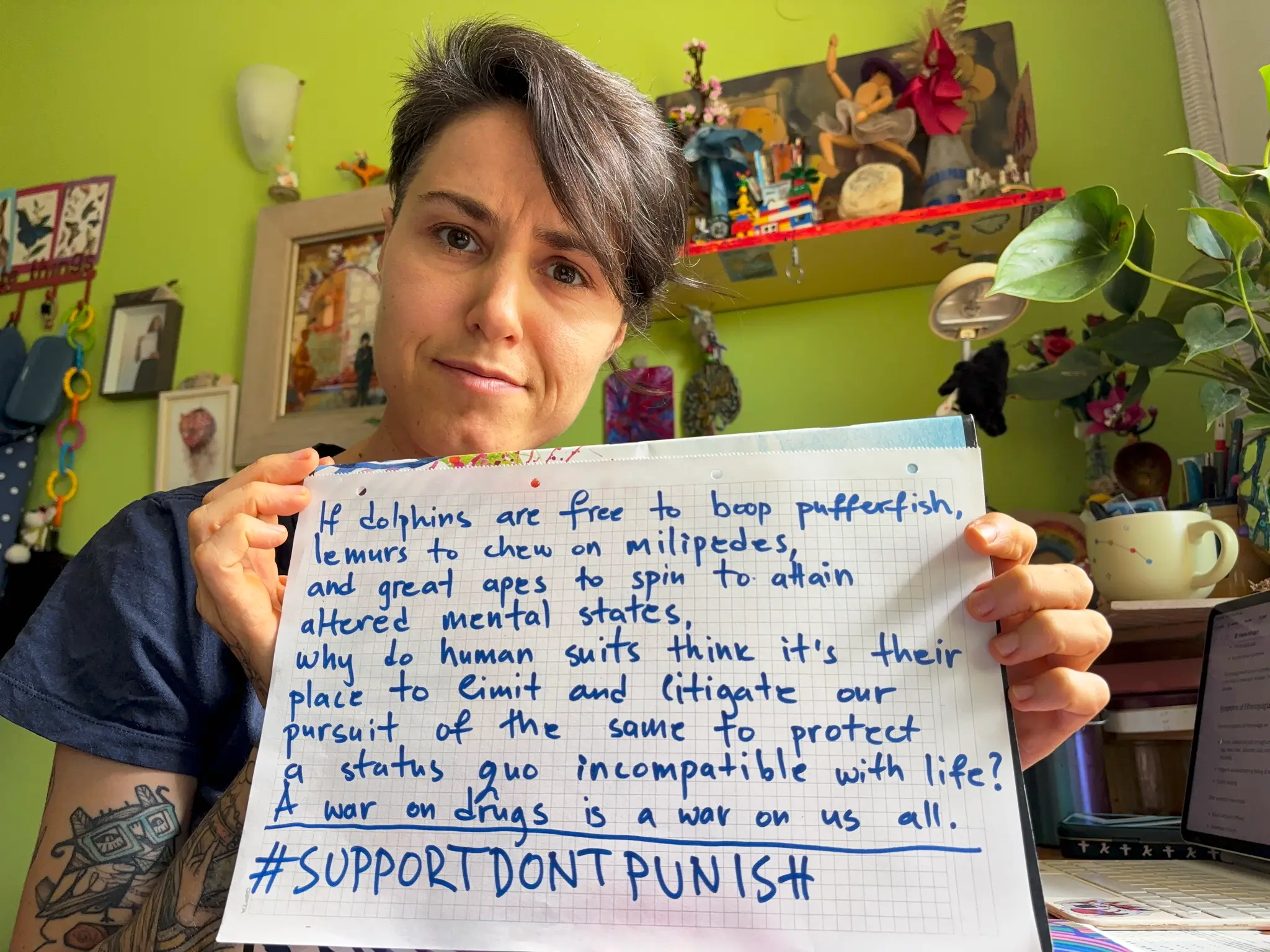 Selfie von Anja Arsovska mit einem Schild in der Handschrift auf Englisch: "If dolphins are free to boop pufferfisch, lemurs to chew on milipedes, and great apes to spin to attain altered mental states, why do human suits htink it's their place to limit and litigate our pursuit of the same to protect a status quo incompatitble with life? A war on drugs is a war on us all. Support Dont Punish." Deutsch in der Bildunterschrift.