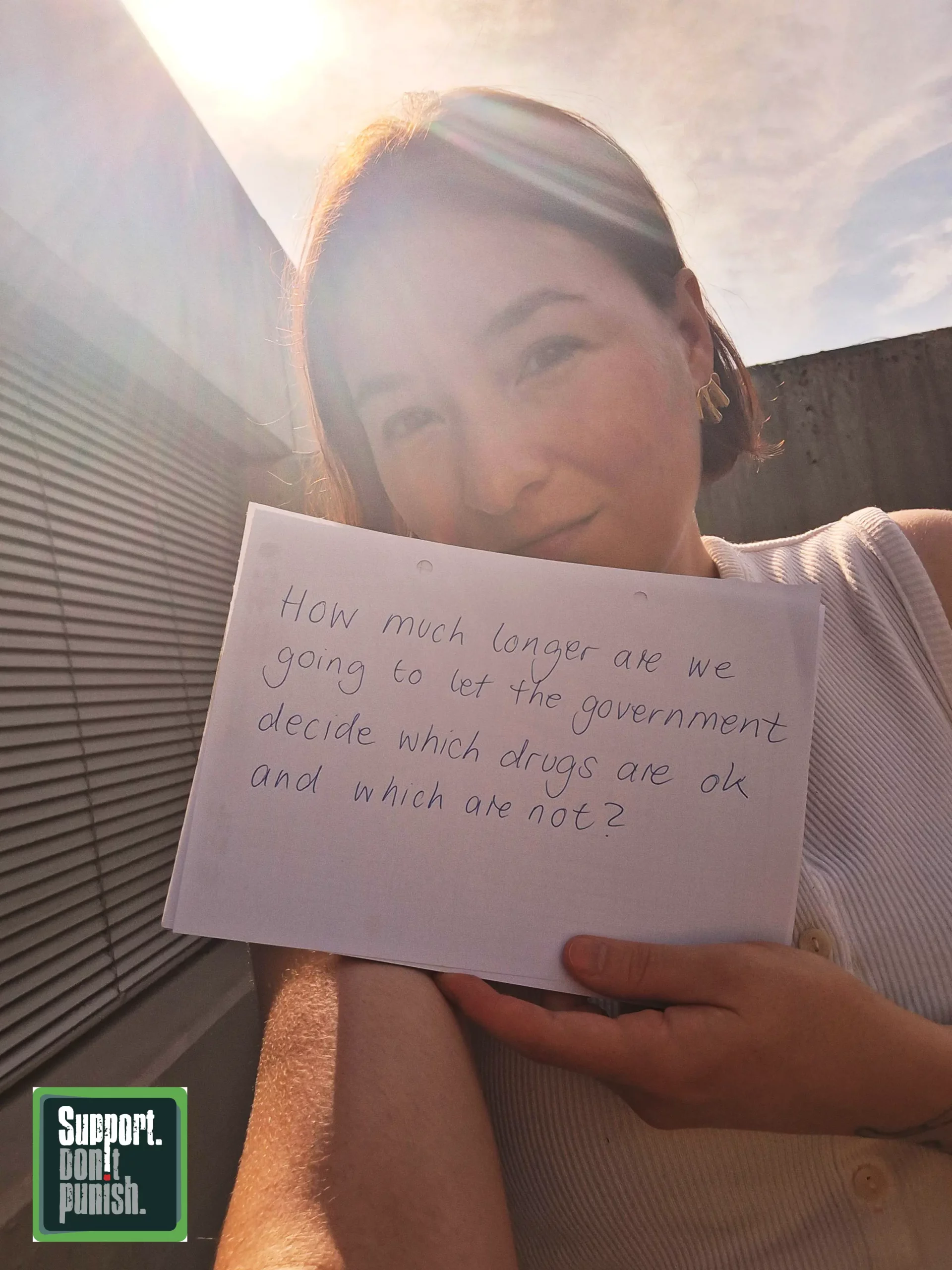 Selfie von Philine Edbauer mit Schild auf Englisch: "How much longer are we going to let the government decide which drugs are ok and which are not?" und dem Logo "Support Dont Punish". Übersetzung in der Bildunterschrift.