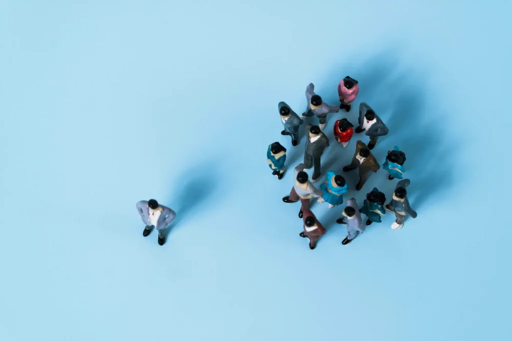 Spielzeugfiguren, fotograpfiert von oben: Eine Gruppe von Menschen schließt einen Einzelnen aus.