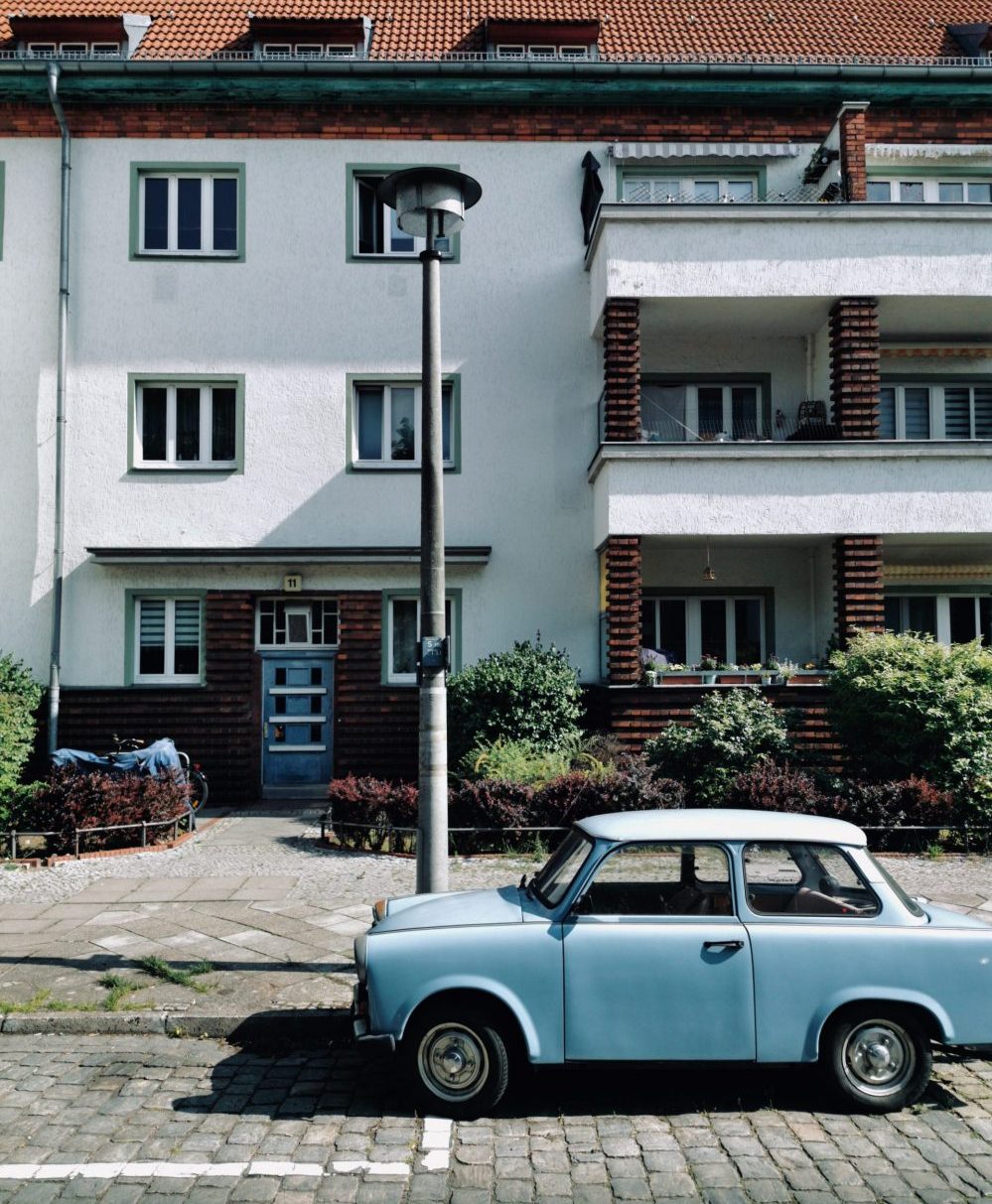Foto-Ansicht am Tag: Ein blauer Trabbi ist vor einem zwei-stöckigen Wohnhaus in Treptow-Köpenick geparkt.